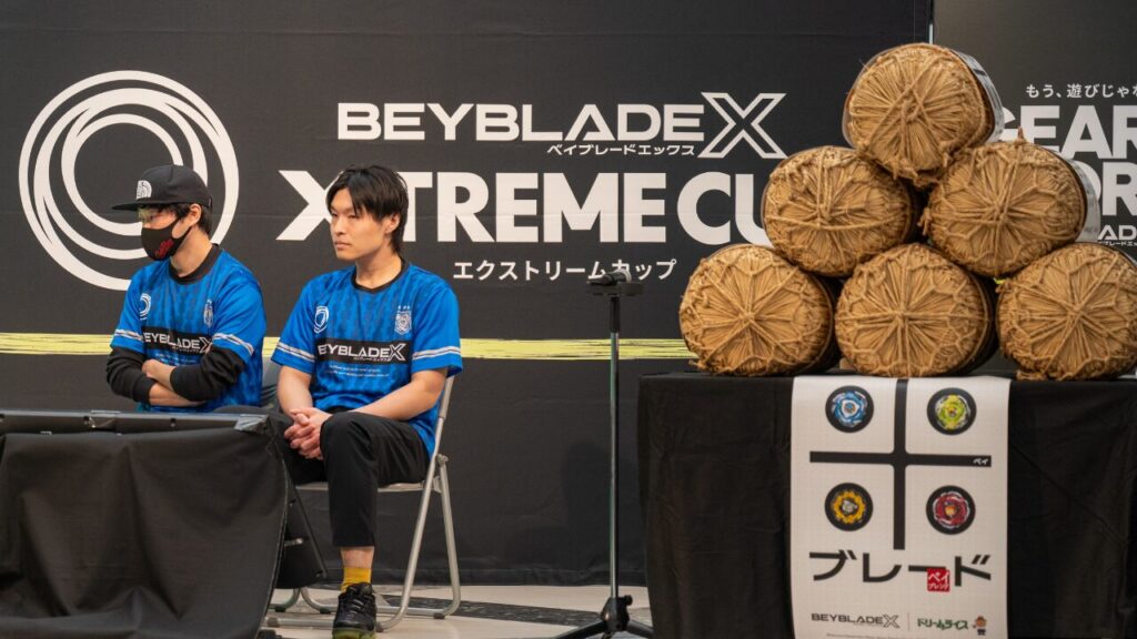 BEYBLADE X XTREME CUPの会場で、とんちゃん・MGr選手がステージ脇で座って待機している