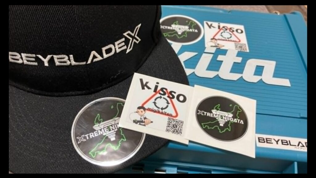 XTREME NIIGATAときっそさんのステッカー、ベイブレードXキャップ、収納ケースが並ぶ様子